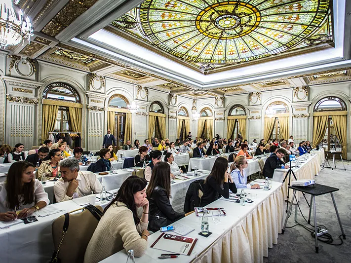 Participanți la mese, cu cupola de vitraliu și candelabrele sălii Le Diplomate deasupra